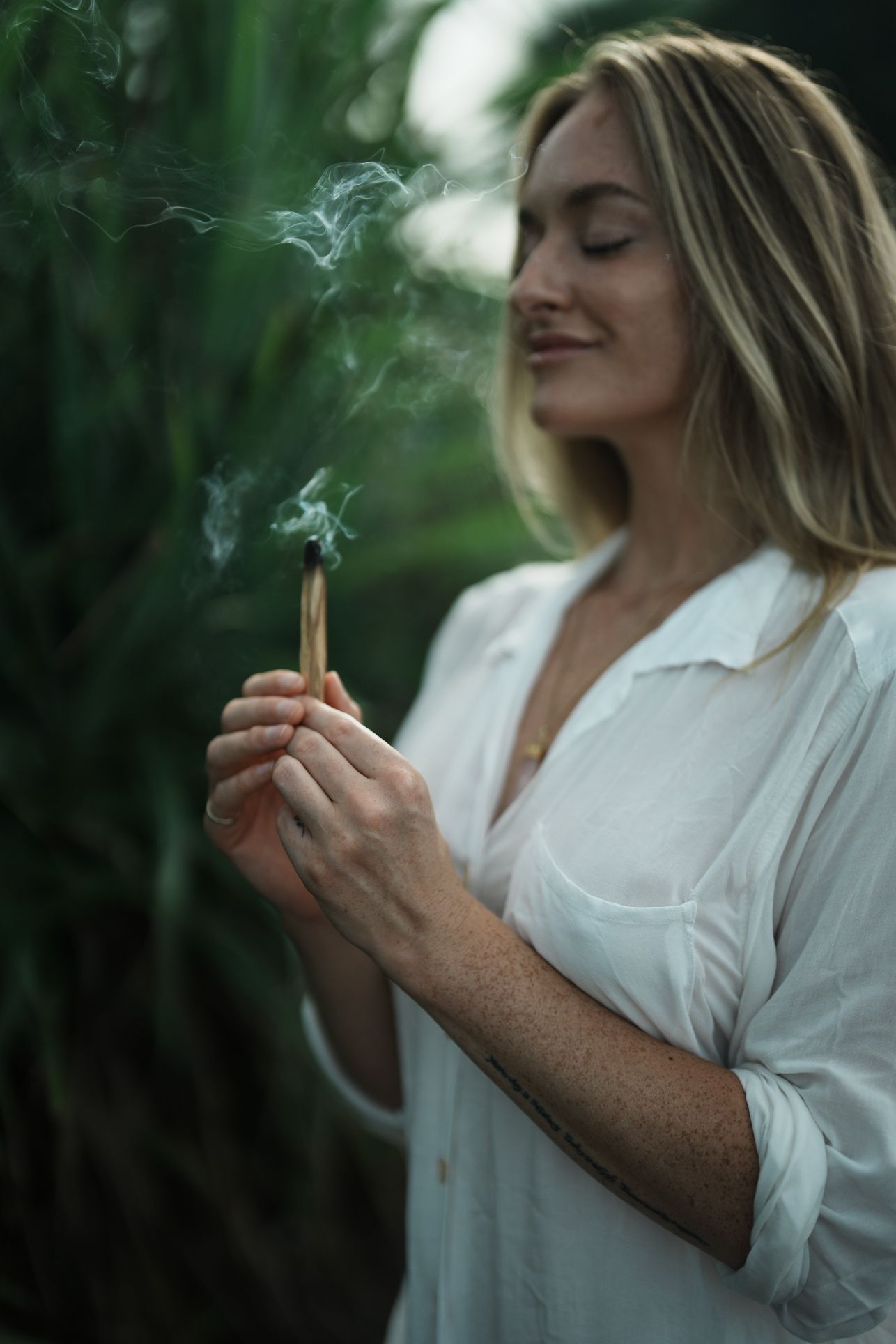 woman wearing white buring palo santo in the balinese jungle