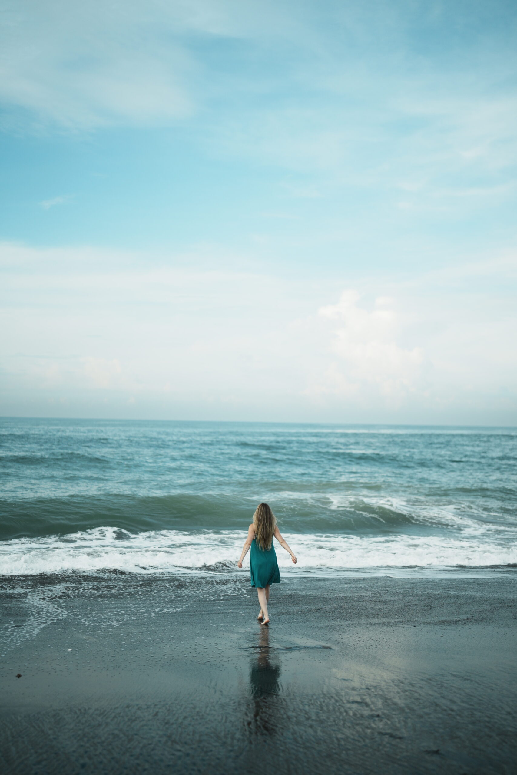 A Woman in a flowing dress, feeling free standing in front of the vibrant blue ocean filling her lungs with a big breathe of fresh air.